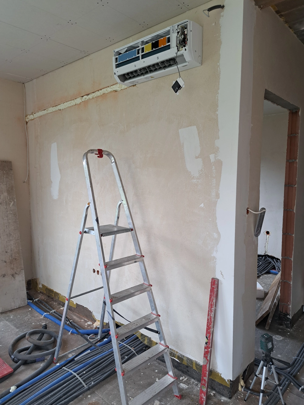 Montaż klimatyzacji – jednostka ścienna z otwartą obudową i przewodami na tle remontowanej ściany