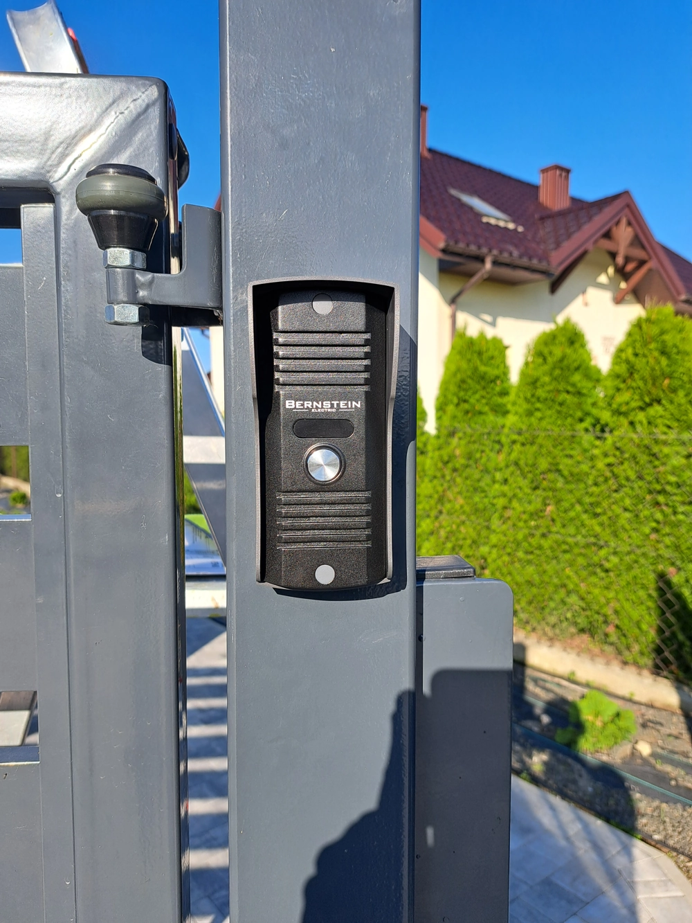 Domofon zamontowany na metalowym słupku w ogrodzeniu przy wjeździe do posesji