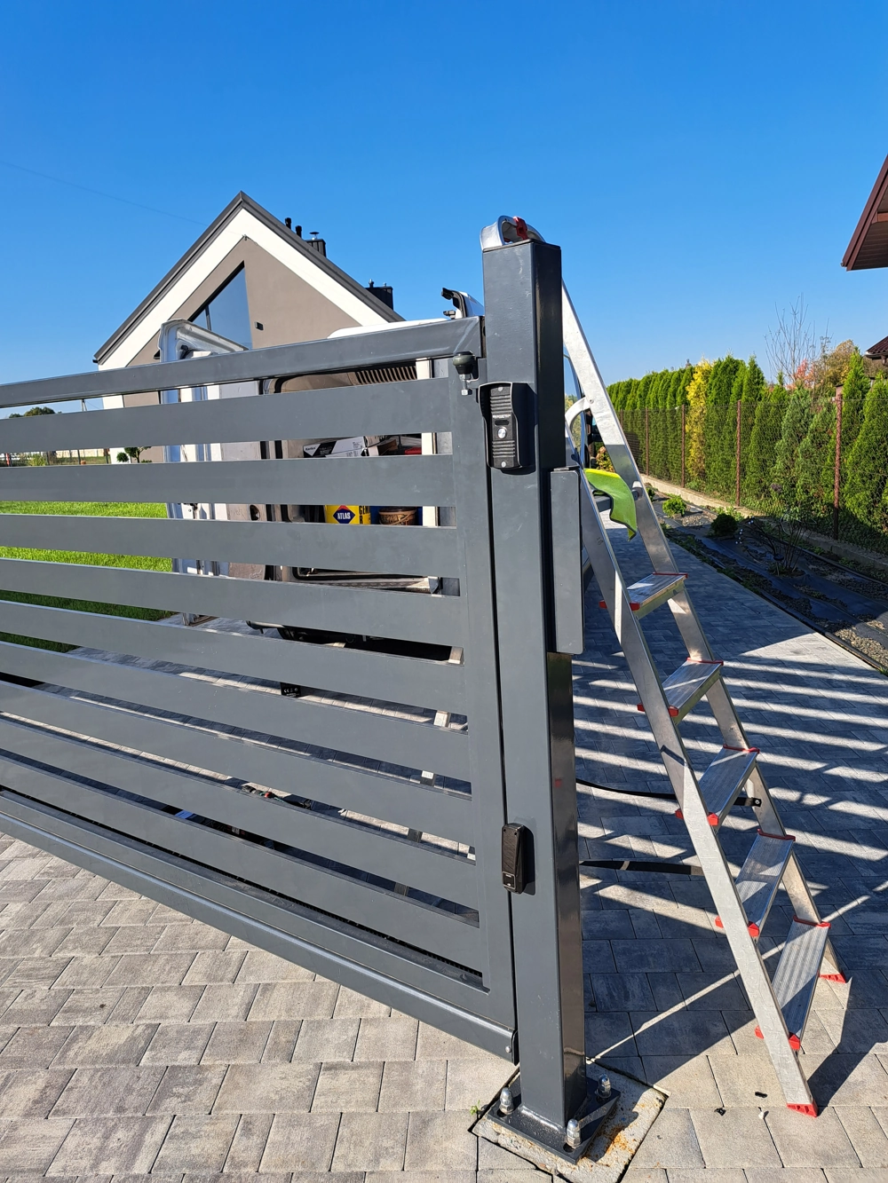 Szara aluminiowa brama przesuwna z poziomymi listwami na podjeździe podczas montażu