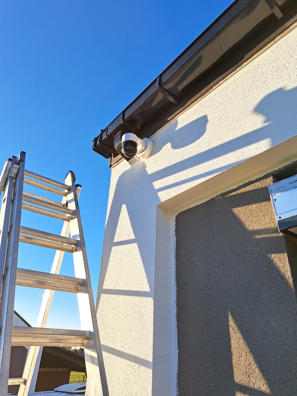 Montaż kamery monitoringu na elewacji domu z użyciem drabiny