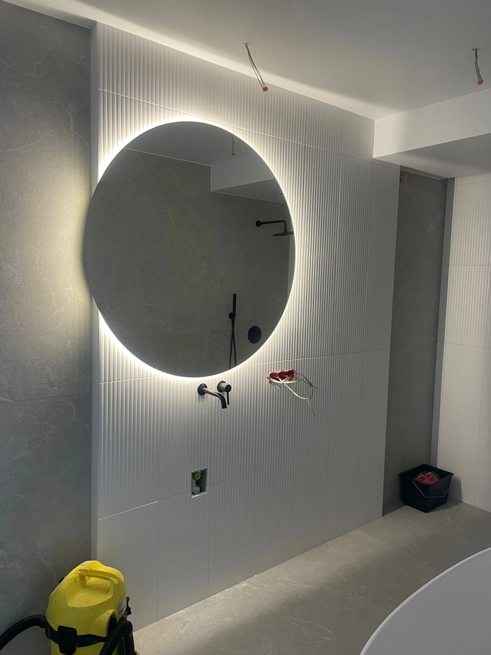 Podświetlane okrągłe lustro łazienkowe z widoczną instalacją elektryczną i przyłączami na białej ścianie, Oświetlenie